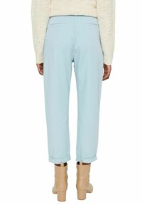 Pantalon bleu clair à coupe décontractée, avec des revers retroussés et des poches arrière. Porté avec des bottines beige à la cheville. Pull en maille texturée visible.