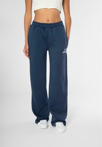 Pantalones de chándal de pierna ancha en azul marino, confeccionados en algodón suave, con cintura elástica y un pequeño logo impreso en blanco en el muslo izquierdo.