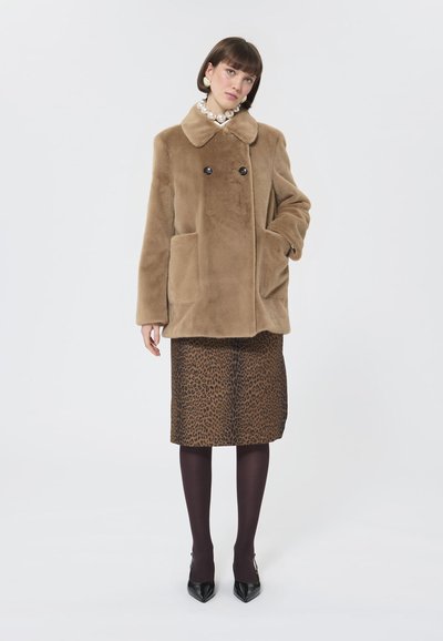 Cappotto in finta pelliccia marrone con ampio colletto, doppi bottoni e tasche laterali, abbinato a una gonna a tubo con stampa leopardata e collant scuri.