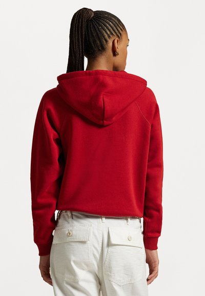 Rød hettegenser med snor i hetta, ribbestrikkede mansjetter og en avslappet passform. Parret med lyse cargo-bukser med knappers baklommer.