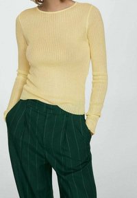 Haut jaune côtelé à manches longues avec un col arrondi, associé à un pantalon à fines rayures vert foncé, doté de poches latérales.