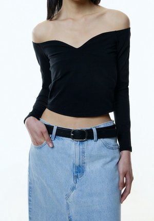 Black long-sleeve off-the-shoulder top with a V neckline, paired with a high-waisted light blue denim skirt and a black belt.