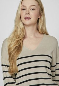 Maglione beige a maglia con scollo a V e righe orizzontali nere, caratterizzato da una vestibilità ampia e un tessuto testurizzato. Maniche lunghe, design leggero.