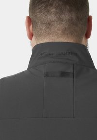 Vista trasera de una persona que lleva una chaqueta oscura de Helly Hansen con el cuello levantado y un pequeño lazo de tela en la parte superior de la espalda.