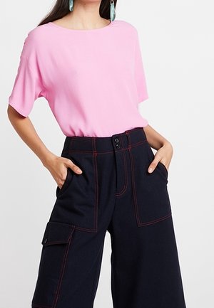 Top rosa de manga corta combinado con pantalones anchos azul marino con costuras rojas, bolsillos delanteros y cierre de botones.