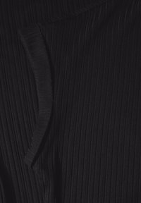 Černá, žebrovaná tkanina zblízka s texturovaným povrchem. Má zakřivený okraj a měkký, jemný lesk. Žádné viditelné vzory ani hardware.