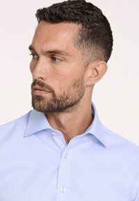 Camicia da uomo azzurro chiaro realizzata in tessuto liscio. Presenta un colletto classico, chiusura con bottoni e una sottile texture. Adatta per occasioni formali.