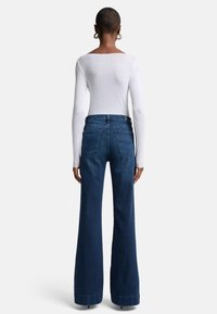 Jeans a vita alta a forma ampia in denim blu scuro, con tasche posteriori, una texture liscia e un orlo pulito con dettagli di cucitura sottili.