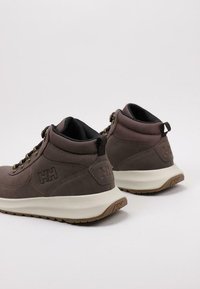 Zapatillas altas marrones de ante y malla, con una mediasuela blanca, acentos texturizados y un logo en el costado y el talón.