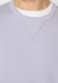 Ljuslila crewneck-tröja med mjuk textur, förstärkt halsringning och subtila sömdetaljer vid axlarna.