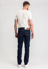 Ciemnoniebieskie dżinsy z denimu o prostym kroju, tylne kieszenie z przeszyciami oraz kontrastowa pomarańczowa skórzana naszywka na pasku.