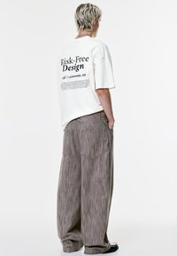 Creme T-shirt med sort tekst på ryggen, sammen med løse, stribede brune bukser. Bukserne har to baglommer. Enkel farvepalette.