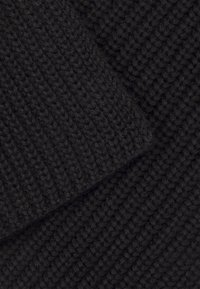 Tessuto nero lavorato a maglia con un motivo testurizzato, che mostra una trama morbida e spessa. Le fibre appaiono pelose, aumentando profondità e calore.