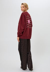 Bordeaux sweatshirt met ronde graphic in roze en witte tekst op de achterkant. Gecombineerd met zwarte broek met luipaardprint en wijde benen. Soepele textuur, ontspannen pasvorm.