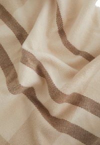 Tela color crema con textura suave que presenta rayas diagonales marrón claro y pliegues suaves.