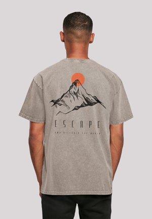Man facing away wearing a gray T-shirt with a black mountain and orange sun graphic and the word "ESCAPE" on the back.