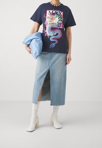 Granatowy t-shirt z nadrukiem smoka, zestawiony z jasną jeansową spódnicą z rozcięciem z przodu oraz białymi botkami na słupku.