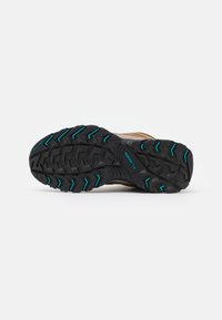 Semelle noire robuste d'une chaussure de randonnée marron avec des accents de traction bleus et la marque « Columbia » sur un fond blanc.