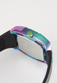 Montre connectée colorée avec une finition métallique arc-en-ciel, un boîtier carré, un bracelet noir texturé et une couronne verte. Dos argenté avec des détails gravés.