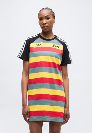 Sieviete valkā īsām piedurknēm kleitu ar horizontālām sarkanām, dzeltenām un zilām svītrām, melnām piedurknēm ar baltām svītrām un uz krūtīm tekstu "Bob".