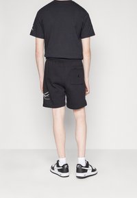 Černé bavlněné tričko a šortky, které mají zadní kapsu a logo na šortkách. Doplňeno černobílými teniskami a bílými ponožkami.