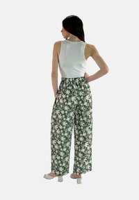 Witte mouwloze top en groene bloemen wijde broek. De broek heeft een wit bloemenpatroon en een elastische tailleband. Blokhak schoenen.