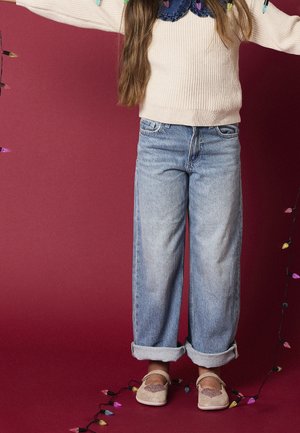 Suéter de punto color beige claro, cuello de mezclilla oscura, jeans de pierna ancha y lavado claro, puños doblados y zapatos crema brillantes con detalles de corazones.