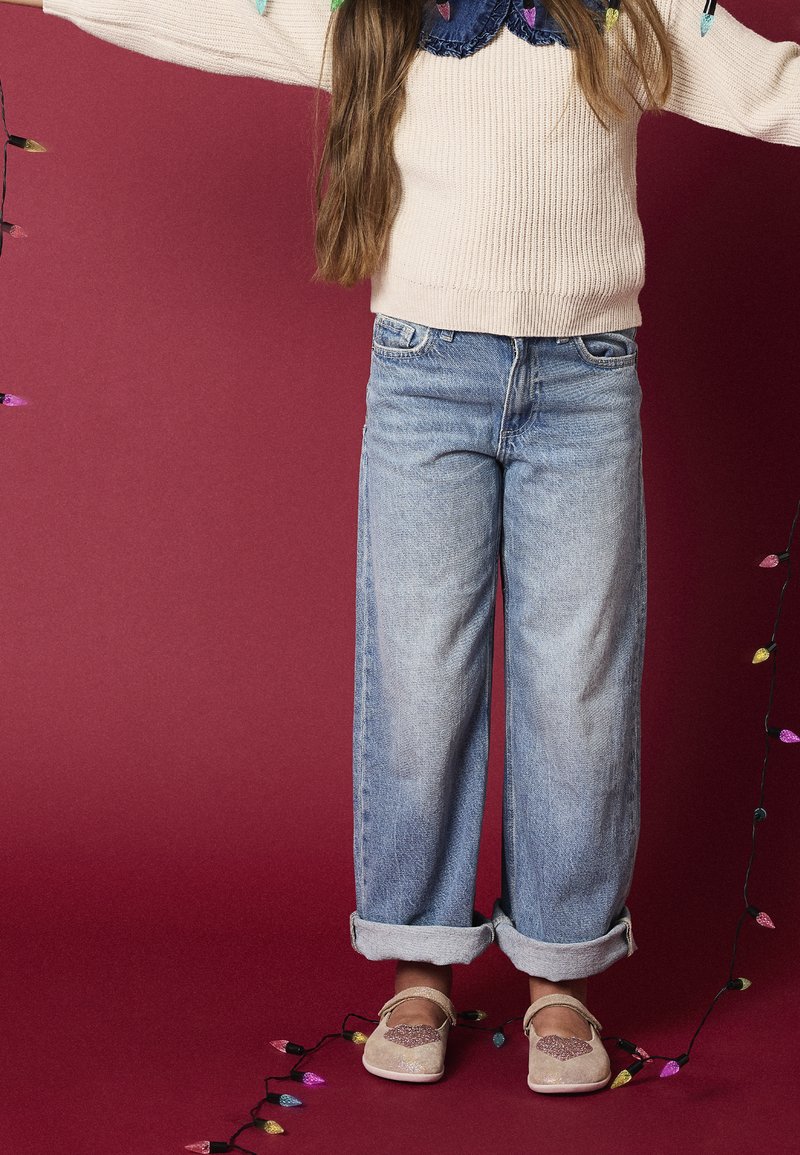 Pull beige clair en tricot, col en jean foncé, jean à jambes larges délavé clair, poignets retroussés et chaussures crème scintillantes avec des accents en forme de cœur.