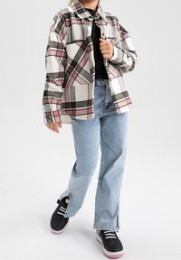 Rutete flannelskjorte med mønstre i rosa, grønt og hvitt, kombinert med lyseblå jeans og svarte joggesko med rosa detaljer.