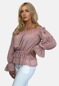 Bluzka off-the-shoulder w delikatnym różowym materiale, z falbaną na dekolcie, elastycznym pasem i rozszerzającymi się rękawami z warstwowym dołem.