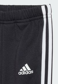 Pantaloni della tuta neri in cotone con tessuto strutturato, cintura elastica e tre strisce bianche lungo i lati con il logo Adidas.