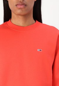 Felpa rossa in morbido cotone con collo a giro. Presenta un piccolo logo ricamato sul petto in blu, bianco e rosso.