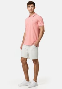 Camisa polo rosa con cuello y mangas cortas, con acentos a rayas. Combinada con pantalones cortos blancos texturizados y zapatillas blancas.