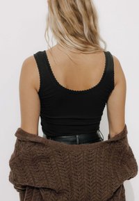 Débardeur noir à côtes avec bords festonnés, associé à un cardigan brun texturé et ample, visible aux épaules et au dos.