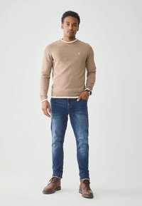 Beige knit sweater with a ribbed hem and white neckline, paired with blue denim jeans and brown leather boots.