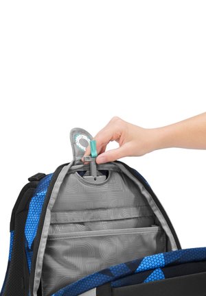 Mano che inserisce un tubo per l’idratazione con una linguetta blu nel vano superiore di uno zaino blu e nero.