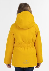 Gul vattentät jacka med insydd midja, huva och elastiska ärmslut. Har logotyp på nedre ryggen och reflexdetaljer på ärmarna.