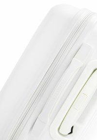 Maleta rígida blanca con un acabado texturizado, cremalleras blancas y un asa lateral con botón de presión. Logo de la marca visible en el lateral.