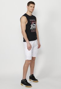 Must musta t-särk, millel on mustade varrukate ja punase ning valge trüki kombinatsioon, koos põlvepikkuste valgete cargo-lühikeste pükstega ja mustade tossudega, millel on kummikummised tallad.