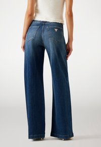 Široké tmavě modré džíny vyrobené z denimu. Obsahují dvě zadní kapsy a malou logo nášivku na pravé kapse. Konec má čistý lem.