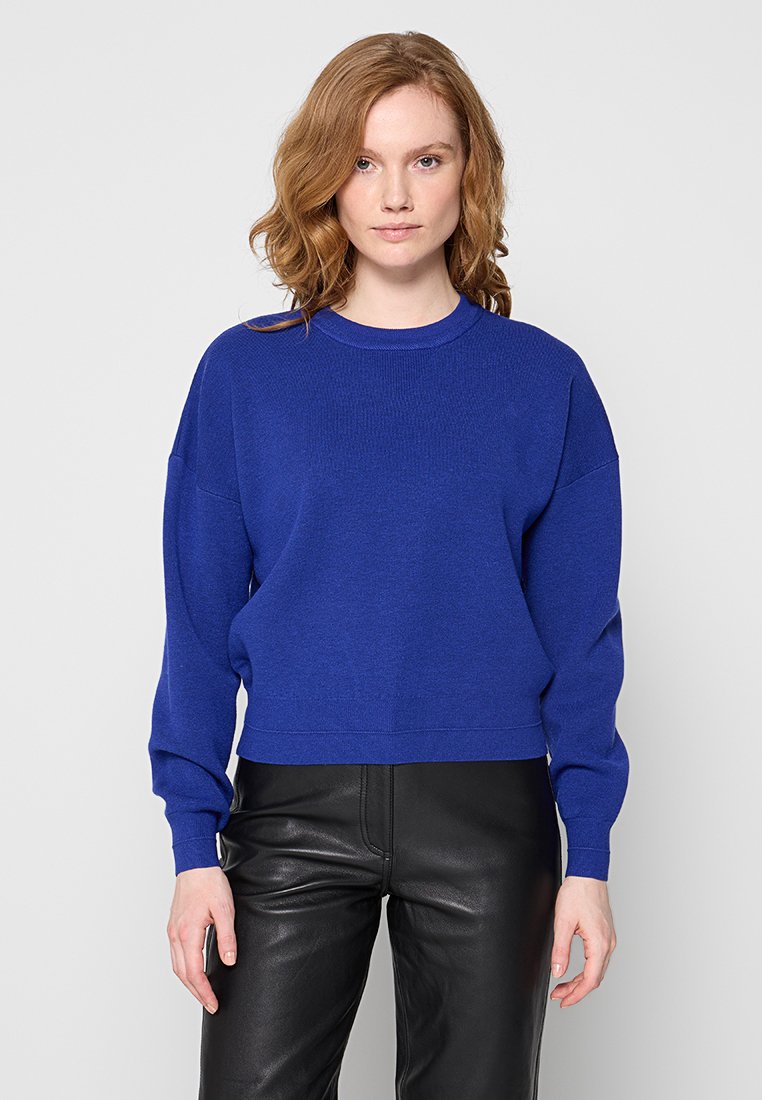 Niebieski sweter dzianinowy z długimi rękawami, ryfoldanym okrągłym dekoltem, luźnym krojem i teksturowanym materiałem. Połączony z czarnymi skórzanymi spodniami.