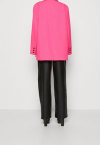 Rosa kavaj med skräddarsydd passform, med långa ärmar och svarta knappaccenter. Kombinerad med höga svarta byxor i imitation läder med vida ben.