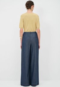 Top corto a maniche corte di un giallo chiaro abbinato a pantaloni larghi blu scuro, caratterizzati da una texture liscia e cuciture a contrasto.