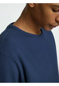 Mörkblå bomullströja med ribbad textur, rund halsringning och synliga sömnadsdetaljer, med fokus på axel- och nackområdet.