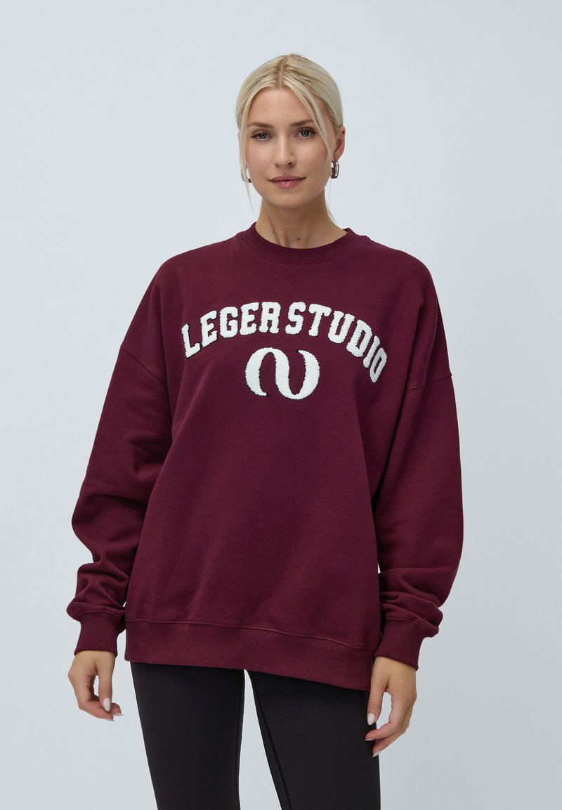 Burgunderfarget oversized sweatshirt med rund hals, med hvit, hevet tekst "LEGERSTUDIO". Glatt tekstur og lange ermer med ribbestrikkede mansjetter.