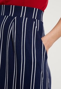 Navy rok met witte verticale strepen, voorzien van een aansluitende tailleband en zijzakken. Gemaakt van zachte stof met een gladde textuur.