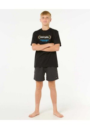 T-shirt en coton noir avec le logo "RIPCURL" en texte coloré, associé à un short de bain gris. Le modèle est pieds nus, debout avec les bras croisés.
