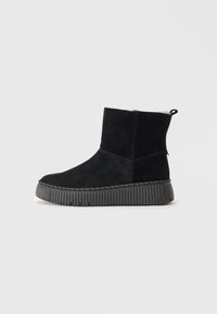 Zwarte suede enkellaars met een gestructureerde zwarte rubberen zool, voorzien van een ronde neus, eenvoudig design en een trekhaak aan de achterkant voor gemakkelijk aan- en uittrekken.