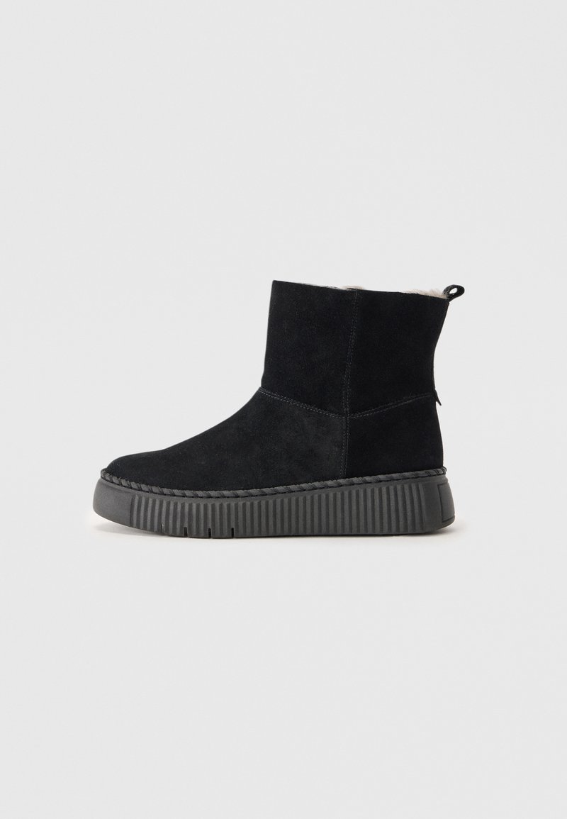 Zwarte suede enkellaars met een gestructureerde zwarte rubberen zool, voorzien van een ronde neus, eenvoudig design en een trekhaak aan de achterkant voor gemakkelijk aan- en uittrekken.