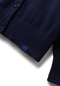 Tmavě námořnický pletený kardigan s žebrovaným lemem, zapínáním na knoflíky a malou látkovou visačkou značky poblíž dolního okraje.